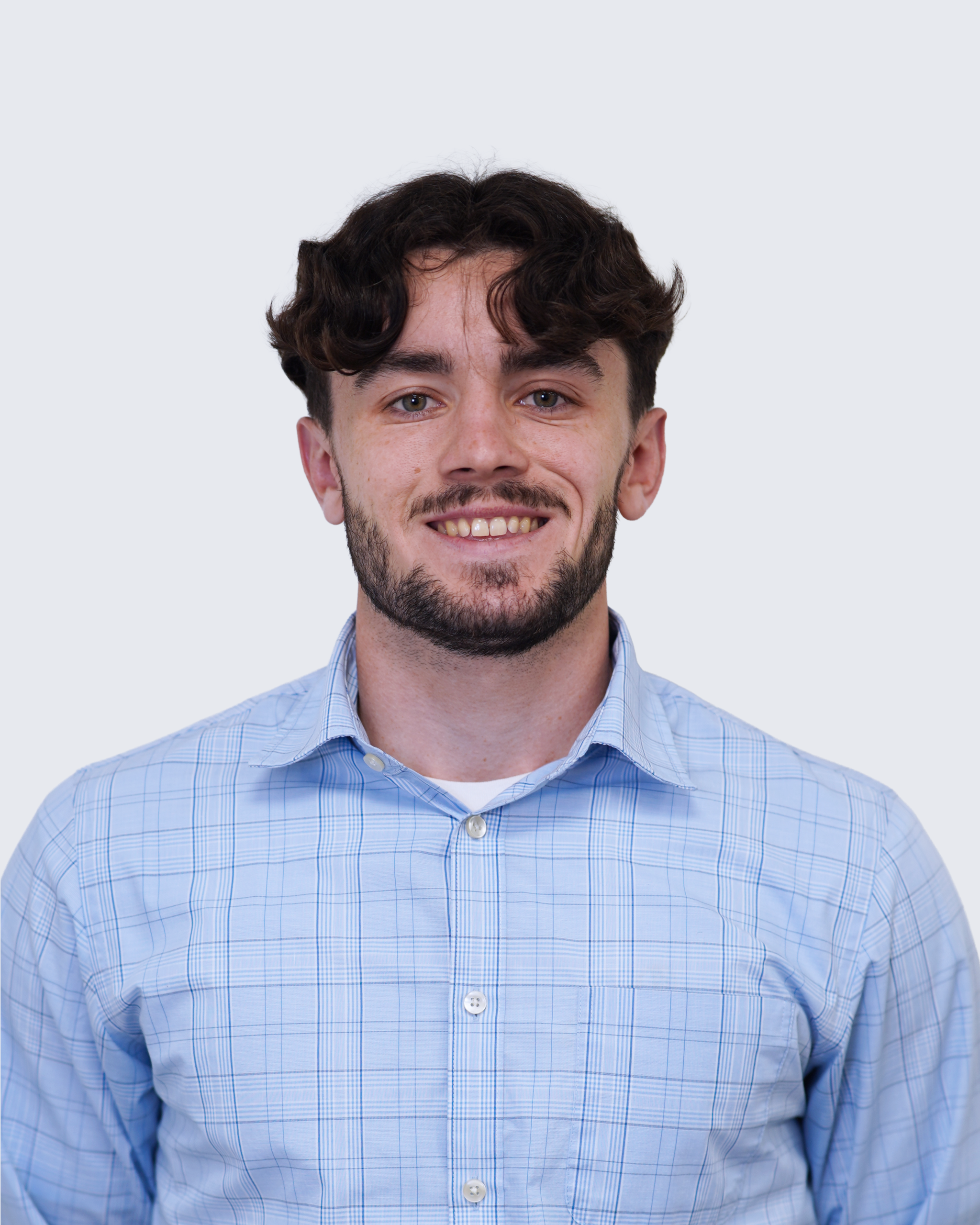 Man with brown hair and beard wearing a light blue checked shirt, standing against a plain light background, looking at the camera and smiling—representing Engineered Systems Inc’s commitment to quality MEP/FP designs.