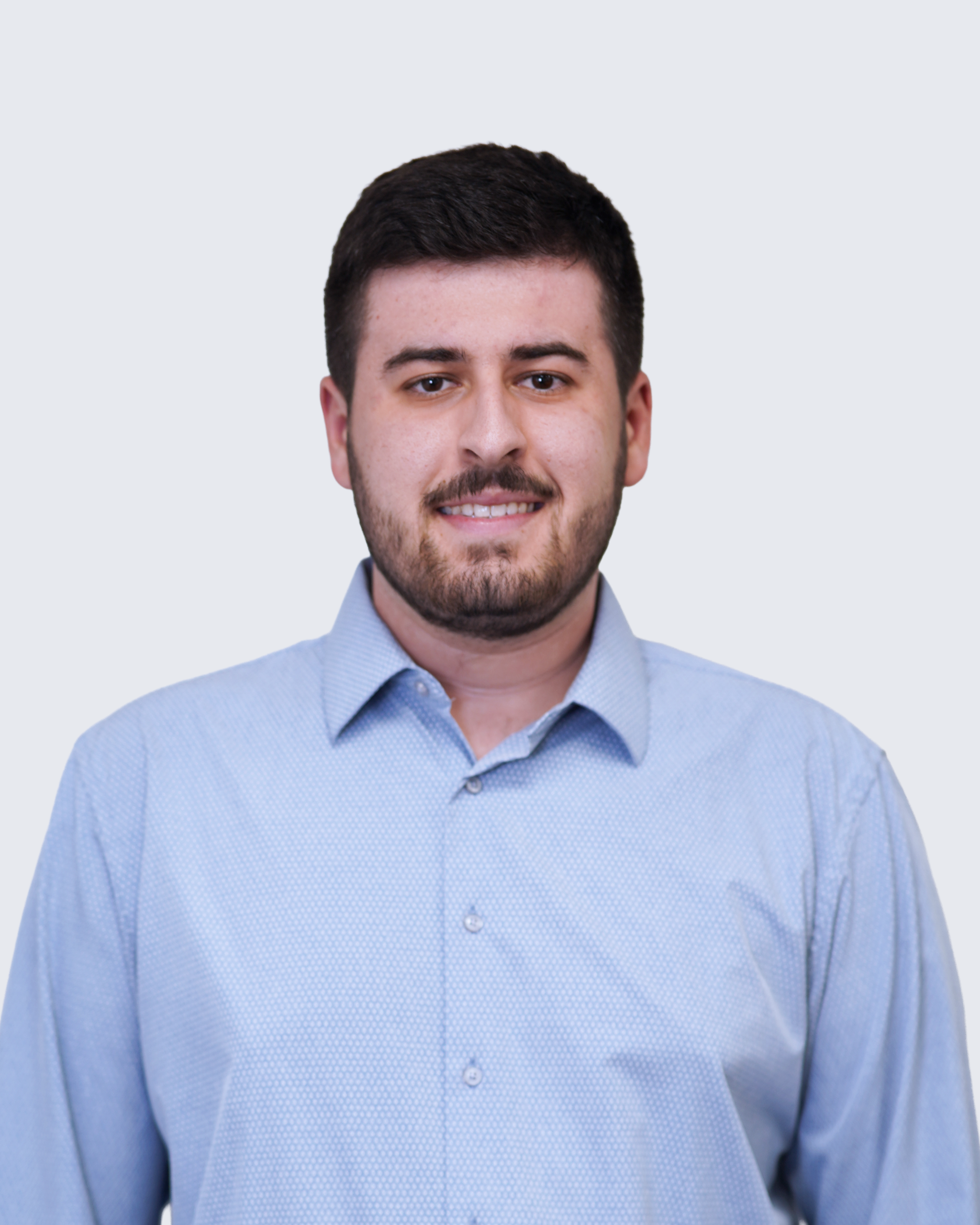 A man with short dark hair and a beard, wearing a light blue button-up shirt, stands against a plain light background, facing the camera and smiling slightly—reflecting the approachable professionalism often associated with MEP/FP designs at Engineered Systems Inc.