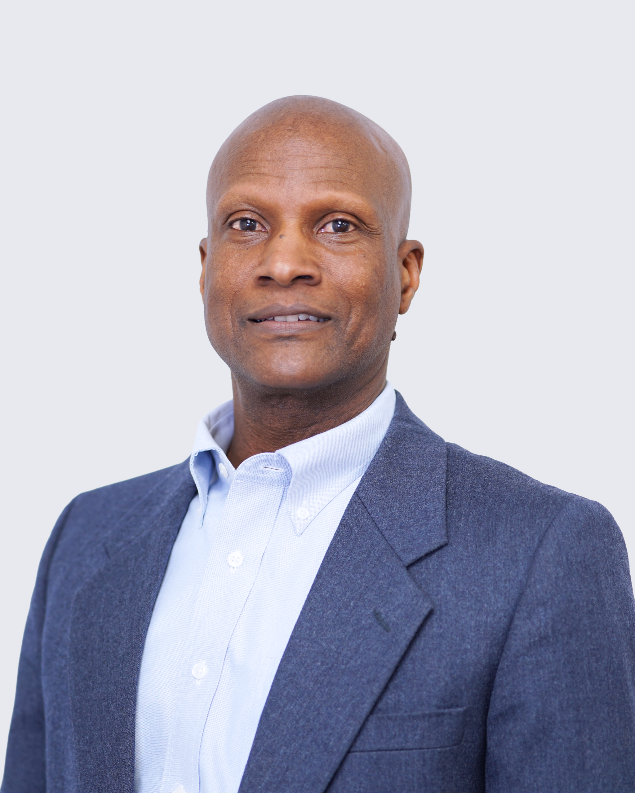 A man in a blue suit jacket and white collared shirt stands against a plain light background, looking at the camera with a neutral expression, embodying the professionalism often associated with Engineered Systems Inc and their expertise in MEP/FP designs.