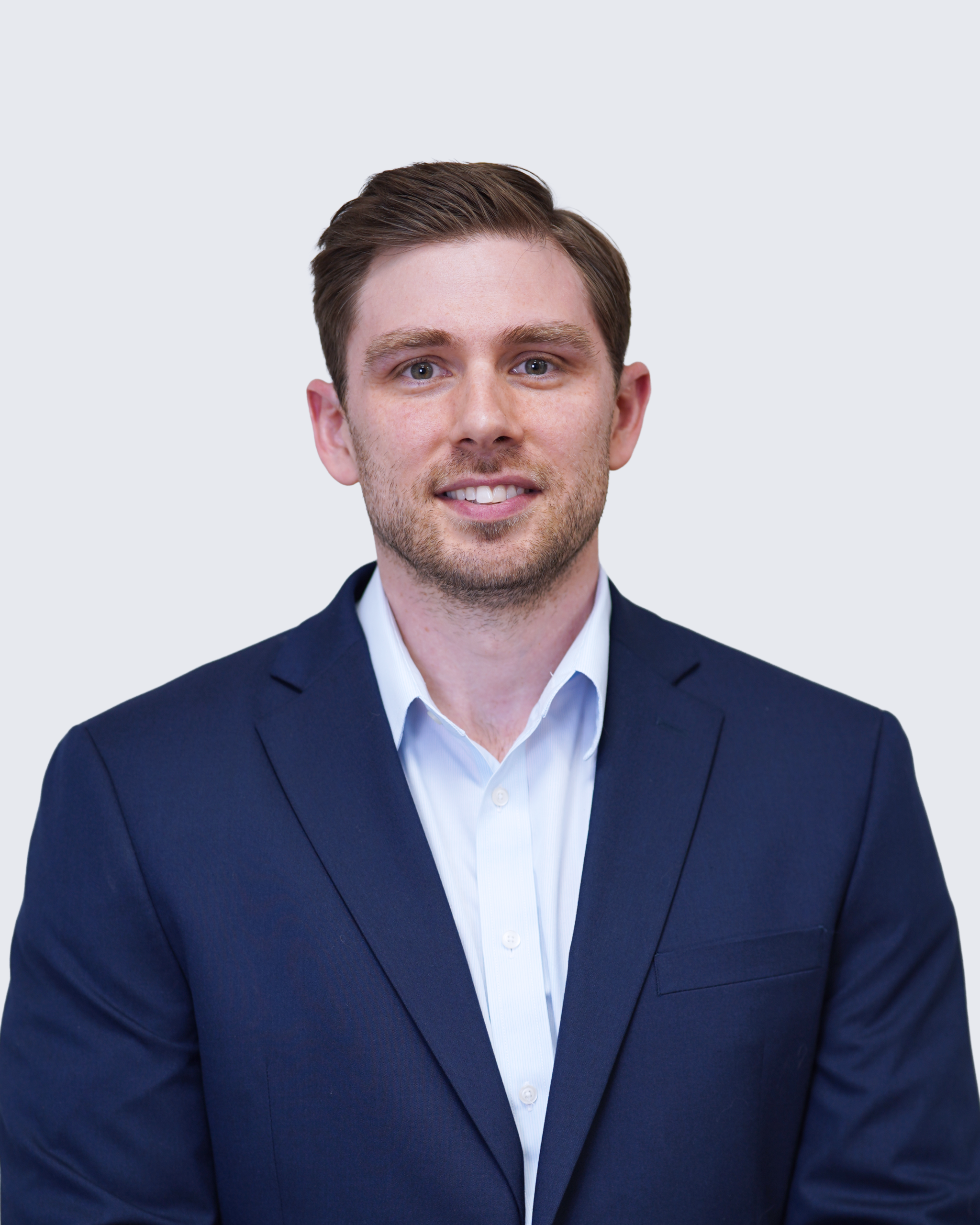 A man in a navy blue suit and light blue shirt stands facing the camera against a plain light gray background, representing Engineered Systems Inc, a leader in innovative MEP/FP designs.