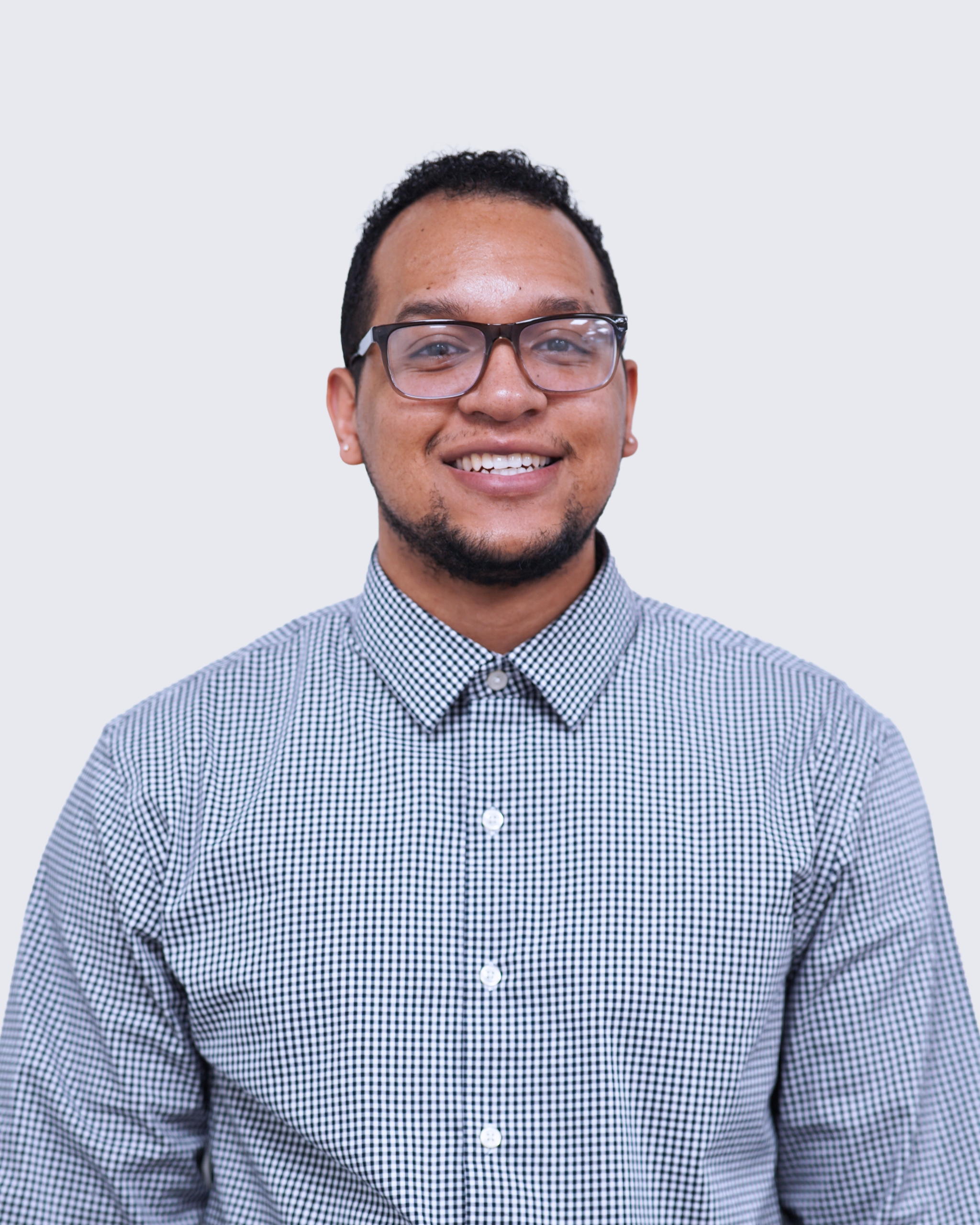 A person wearing glasses and a checkered button-up shirt smiles while facing the camera against a plain light background, embodying the professional spirit of Engineered Systems Inc and their expertise in MEP/FP designs.