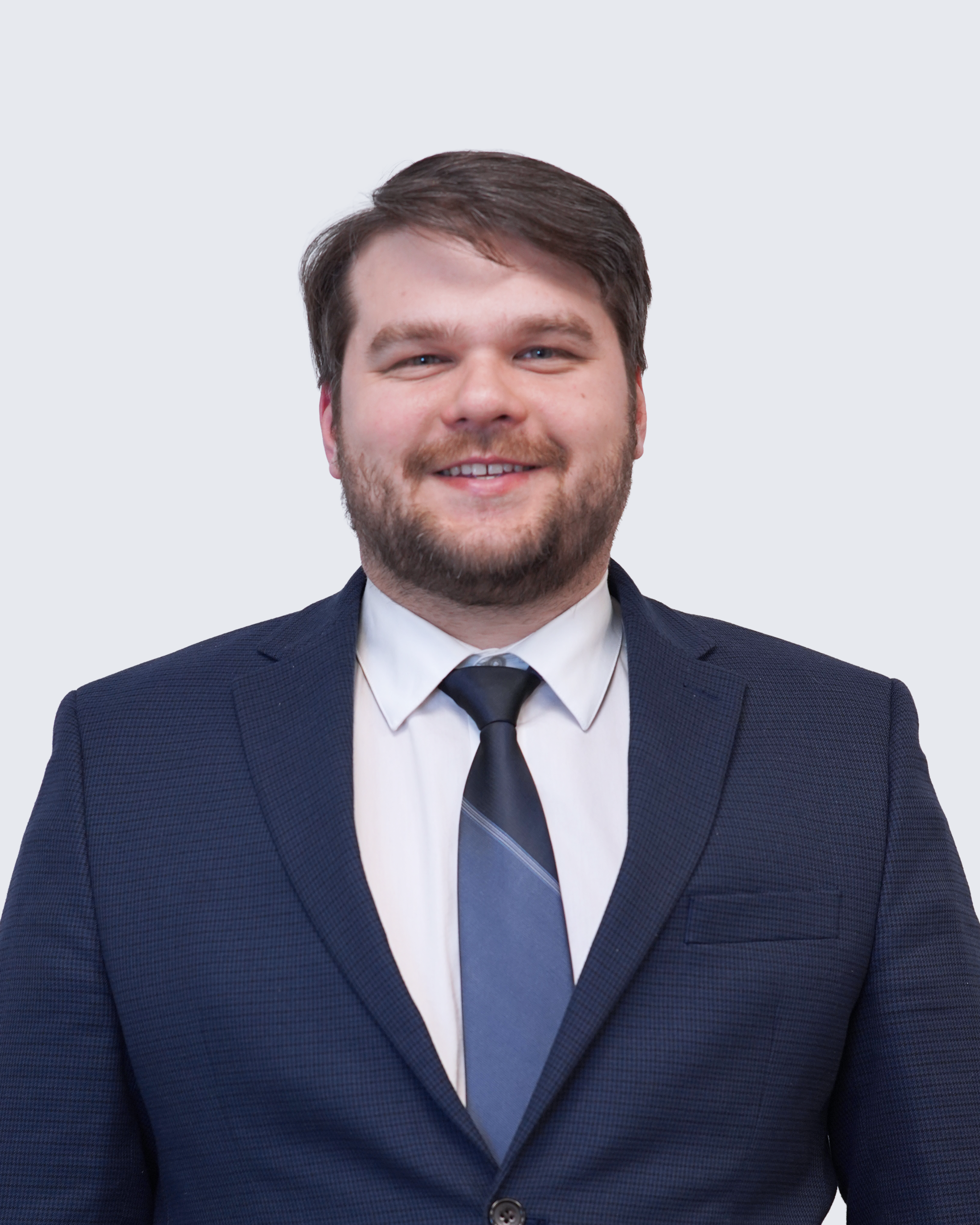 Man wearing a navy blue suit, white shirt, and blue tie, standing against a plain light background, smiling at the camera—a professional representative of Engineered Systems Inc, specializing in MEP/FP designs.