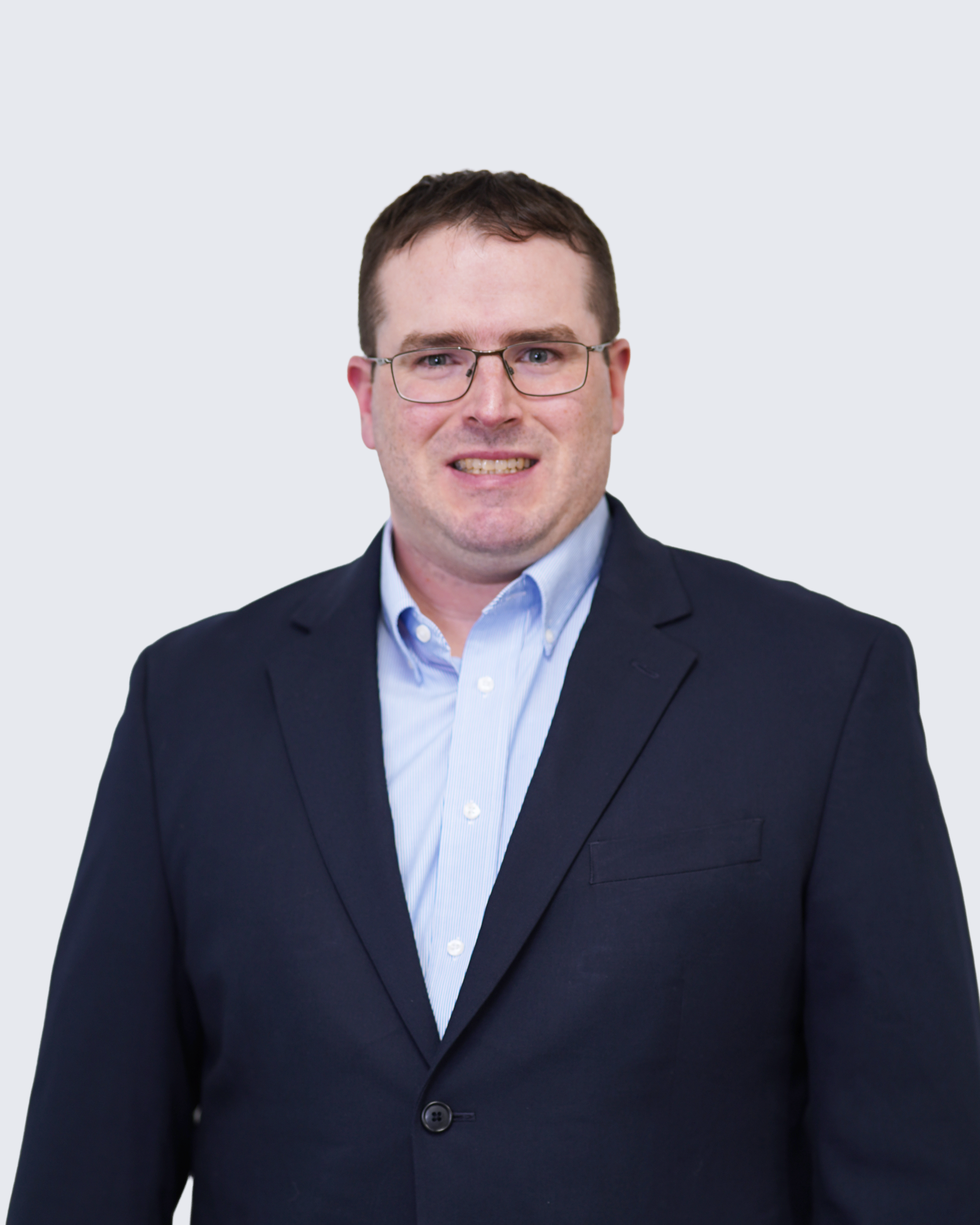 A man with short brown hair, glasses, and a navy suit jacket over a light blue shirt stands against a plain light background, representing Engineered Systems Inc and their expertise in MEP/FP designs.